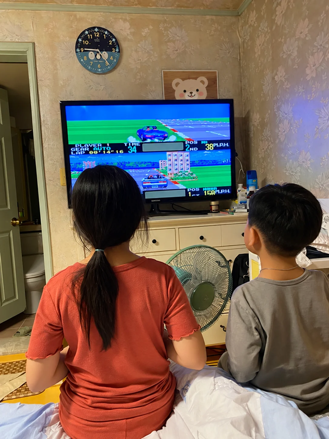 화면이 위아래로 나뉜 자동차 게임을 TV로 함께 즐기는 두 아이의 뒷모습